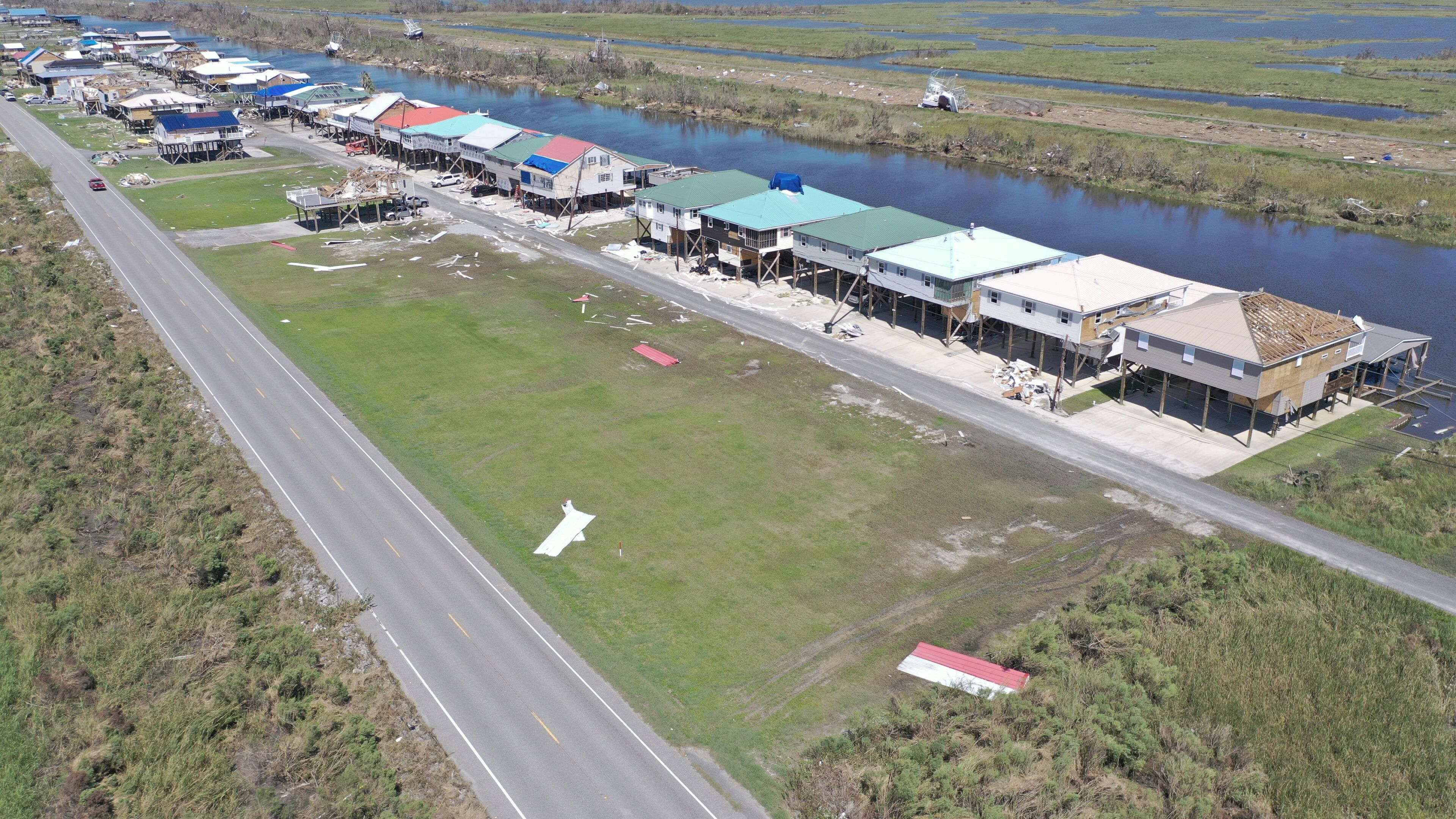 An aerial view of a waterfront community with houses on stilts, a road, and a river.