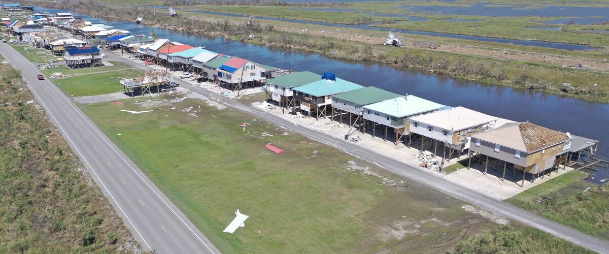 An aerial view of a waterfront community with houses on stilts, a road, and a river.