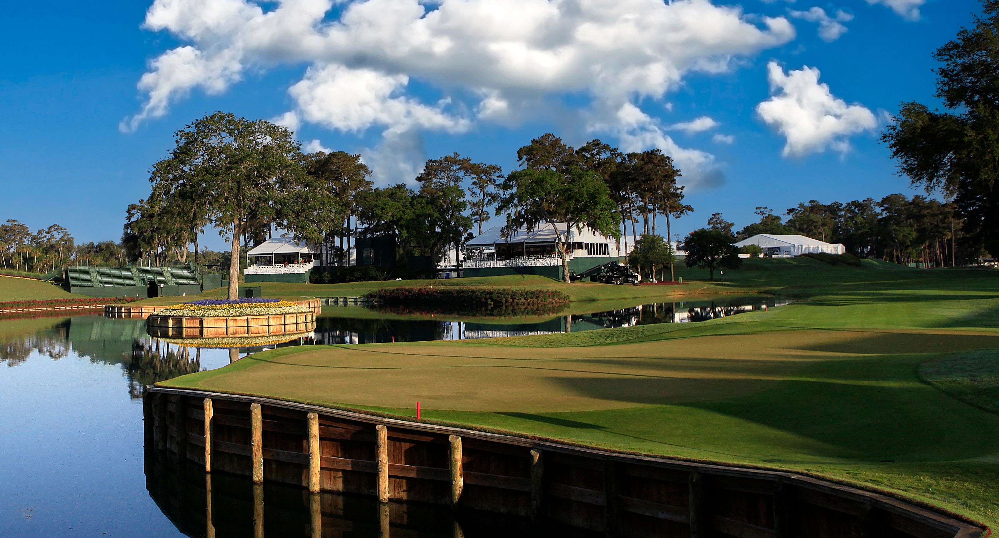 A golf course with a pond, trees, and buildings in the background.