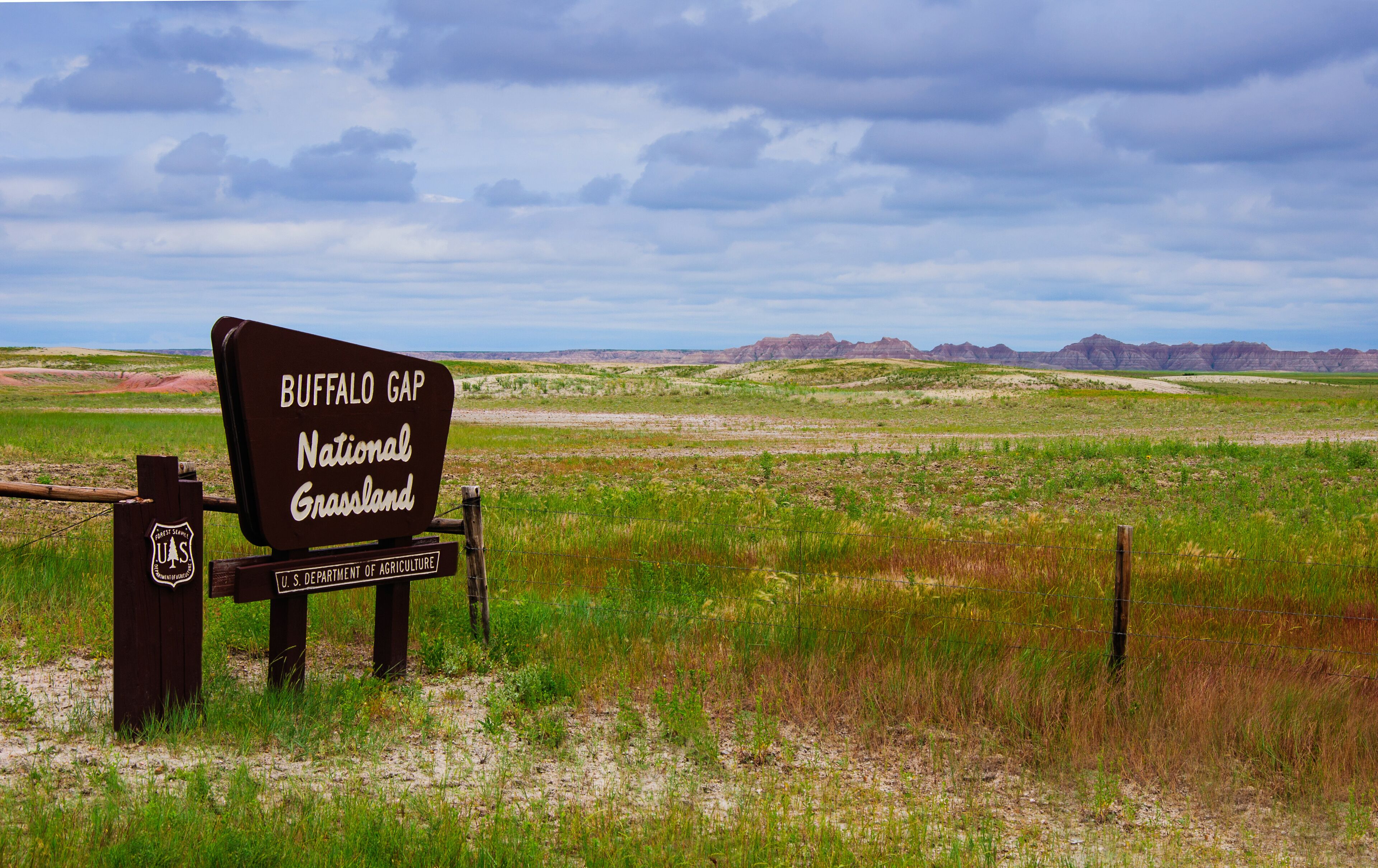 A sign for Buffalo Gap National Grassland with a vast prairie landscape and distant mountains.