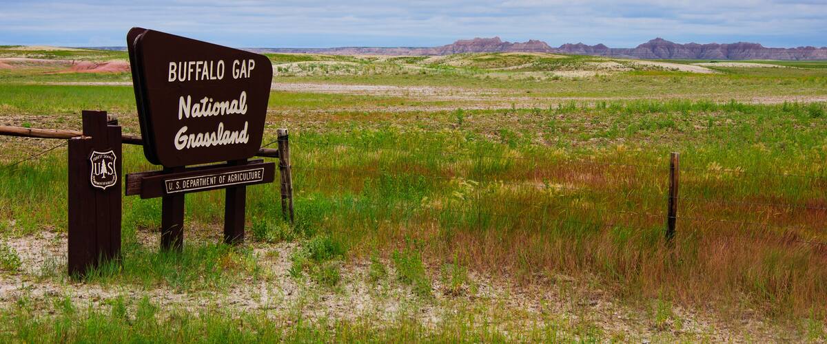 A sign for Buffalo Gap National Grassland with a vast prairie landscape and distant mountains.