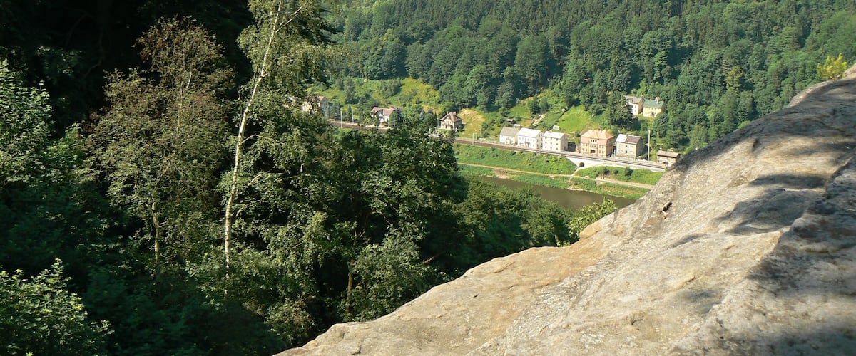 A valley with dense forests, a river, and a castle-like building on a hill.