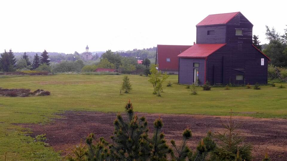 A rural landscape with a large barn, a smaller red building, and a distant church.