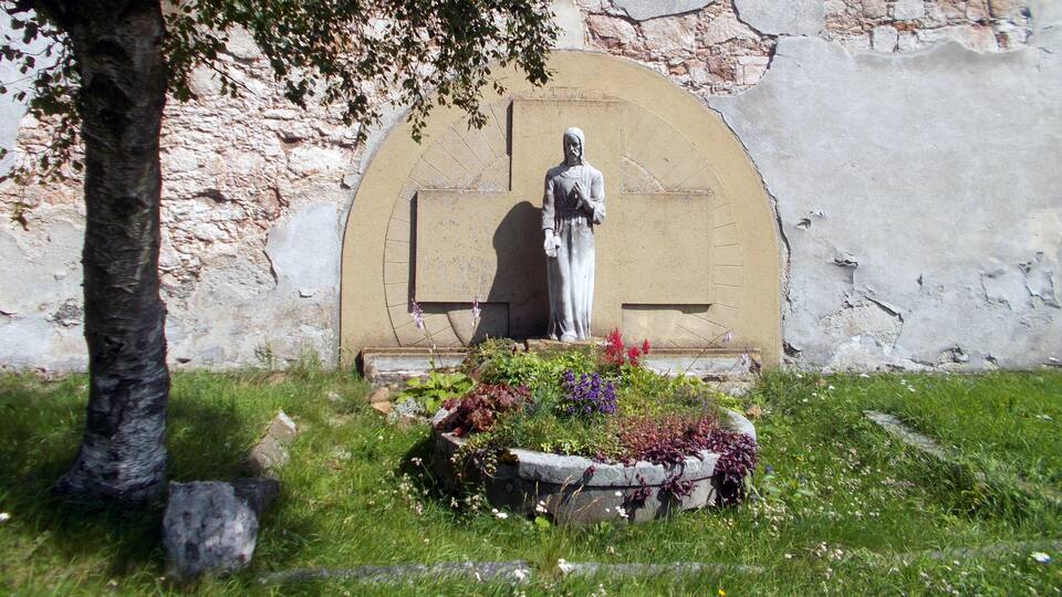 A statue in a garden with a stone wall in the background.