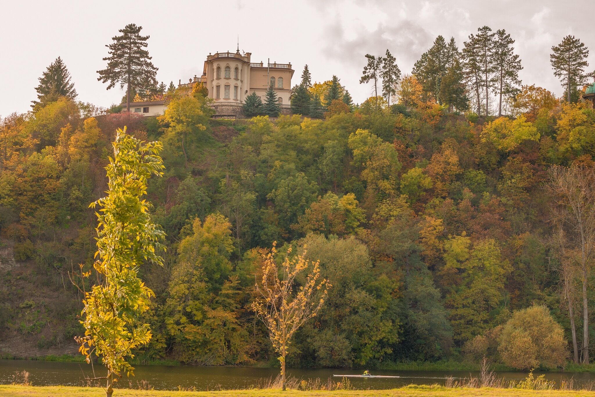 A castle on a hill, surrounded by autumn-colored trees and a lake.