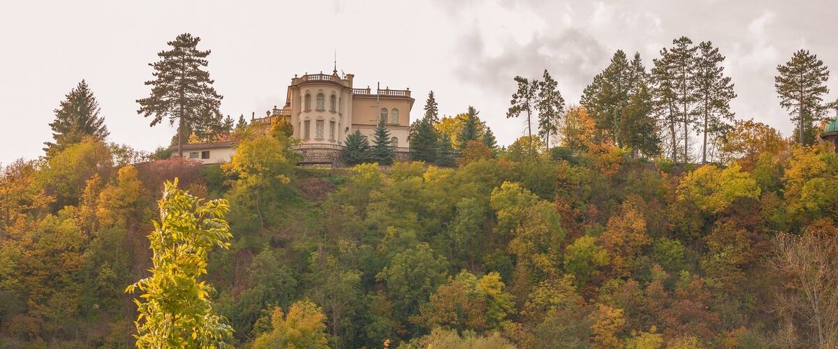 A castle on a hill, surrounded by autumn-colored trees and a lake.