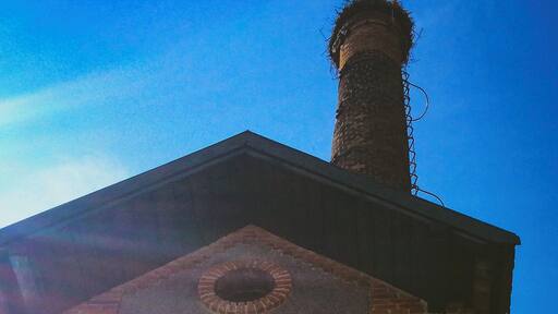 Un edificio de ladrillo con una chimenea, un ventanal circular y una puerta.