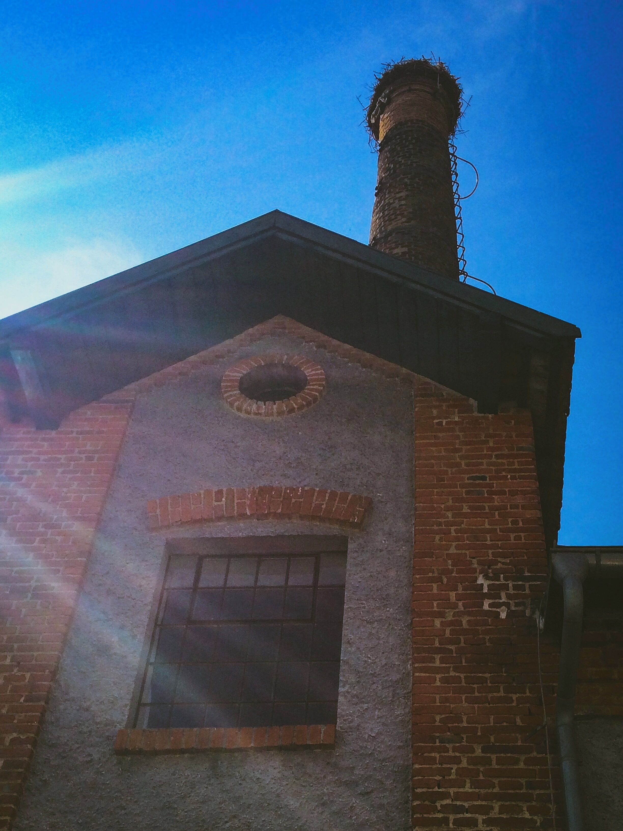 A brick building with a chimney, a circular window, and a door.