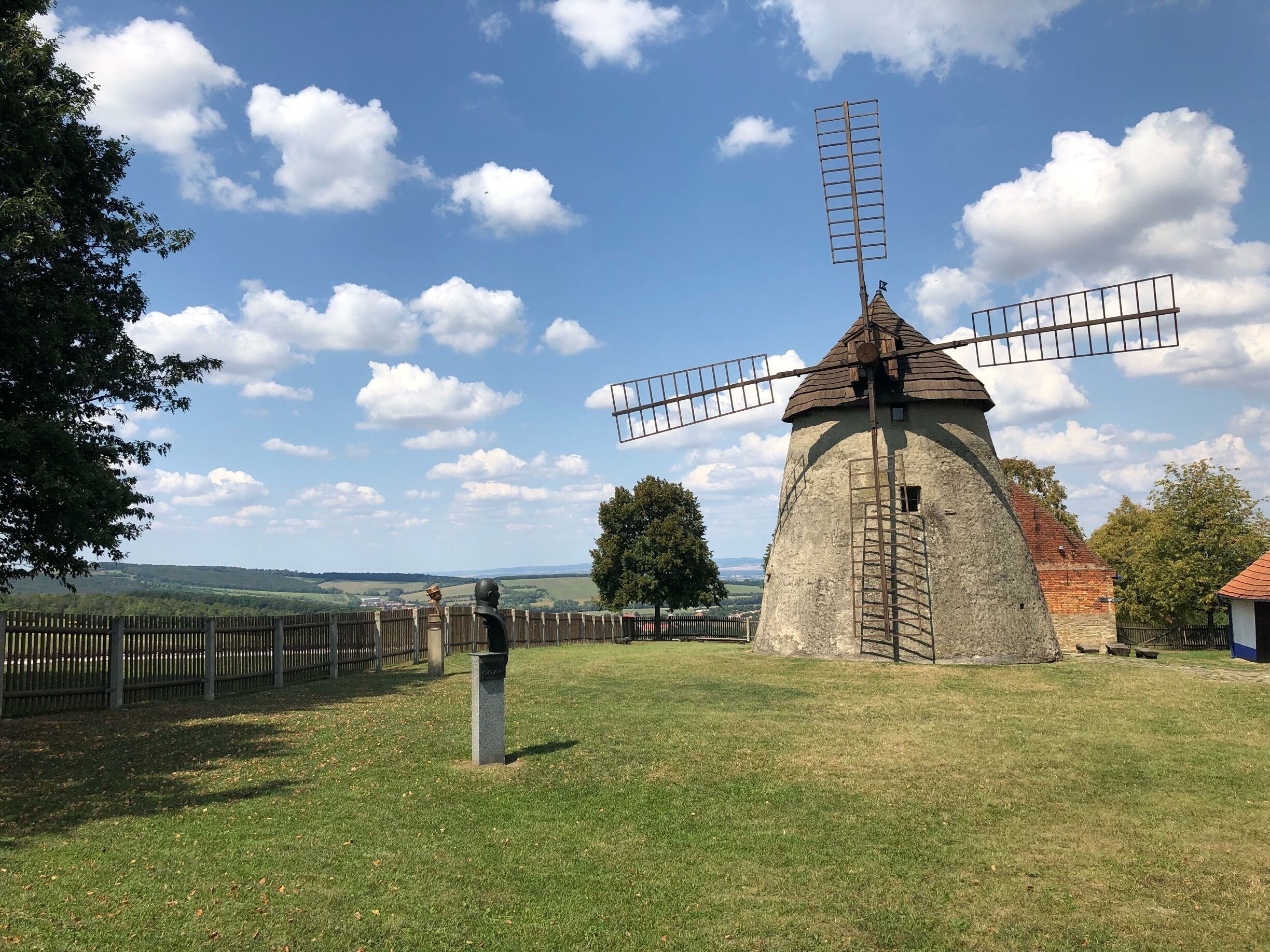 A traditional windmill with a wooden fence in the foreground and a clear blue sky with clouds in the background.