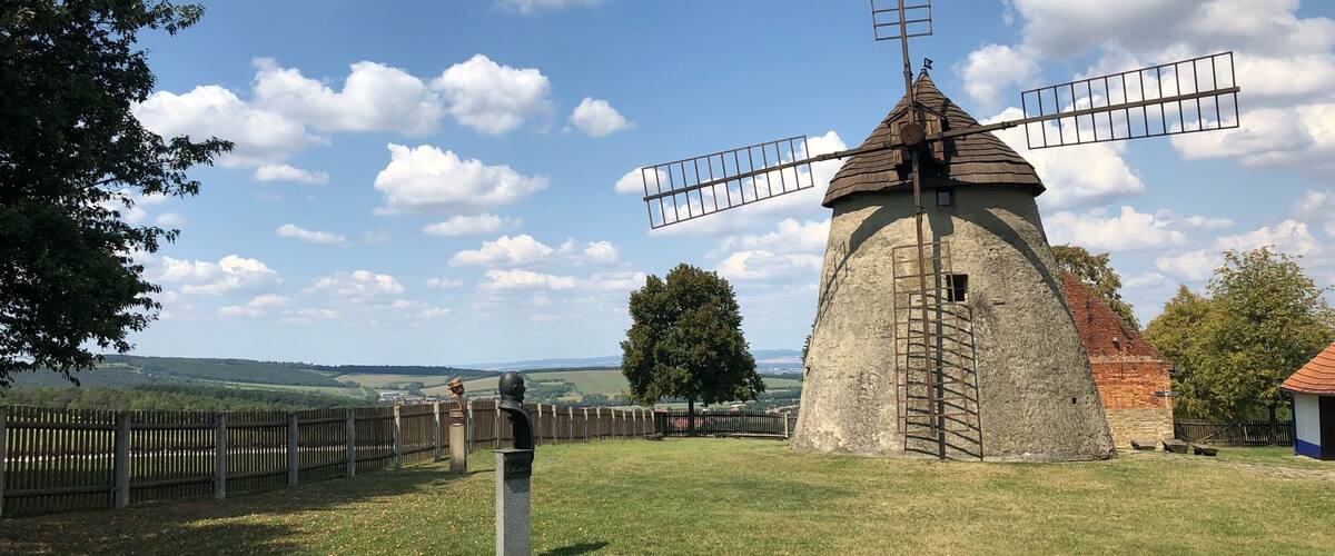 A traditional windmill with a wooden fence in the foreground and a clear blue sky with clouds in the background.