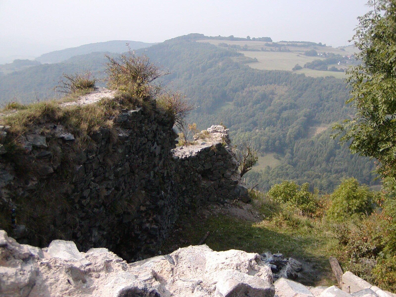 A rocky cliff edge overlooking a valley with dense forest and rolling hills in the background.