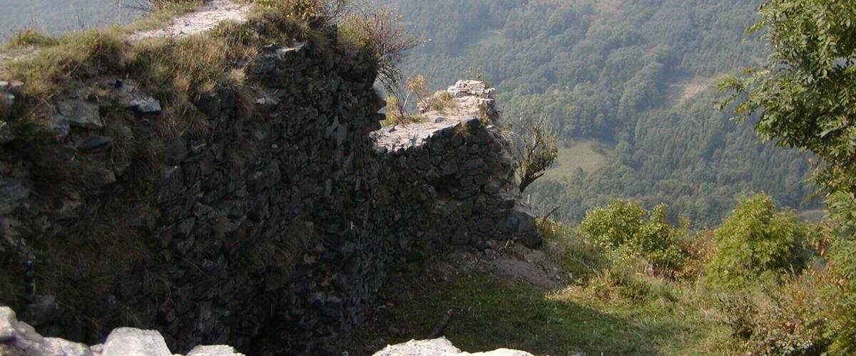 A rocky cliff edge overlooking a valley with dense forest and rolling hills in the background.