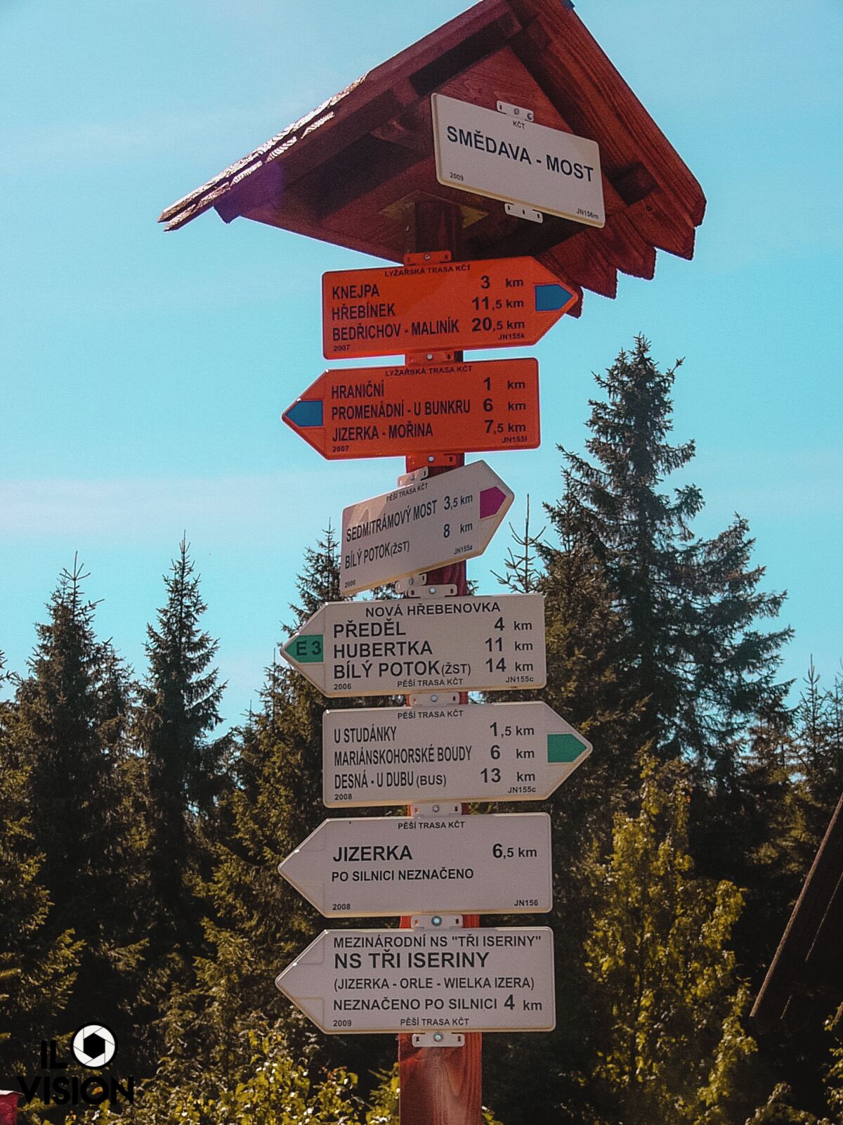A wooden signpost with multiple directional signs in a forested area.