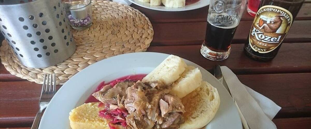 A plate of food with meat and potatoes, a glass of beer, and a bottle of beer on a wooden table.