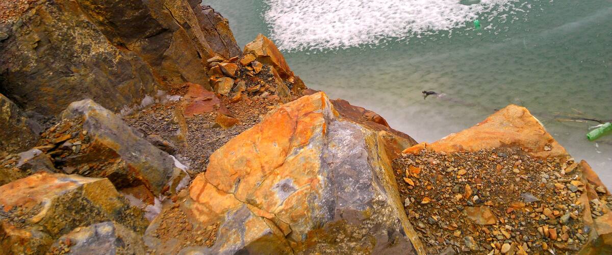 A rocky shoreline with clear water and a person swimming.
