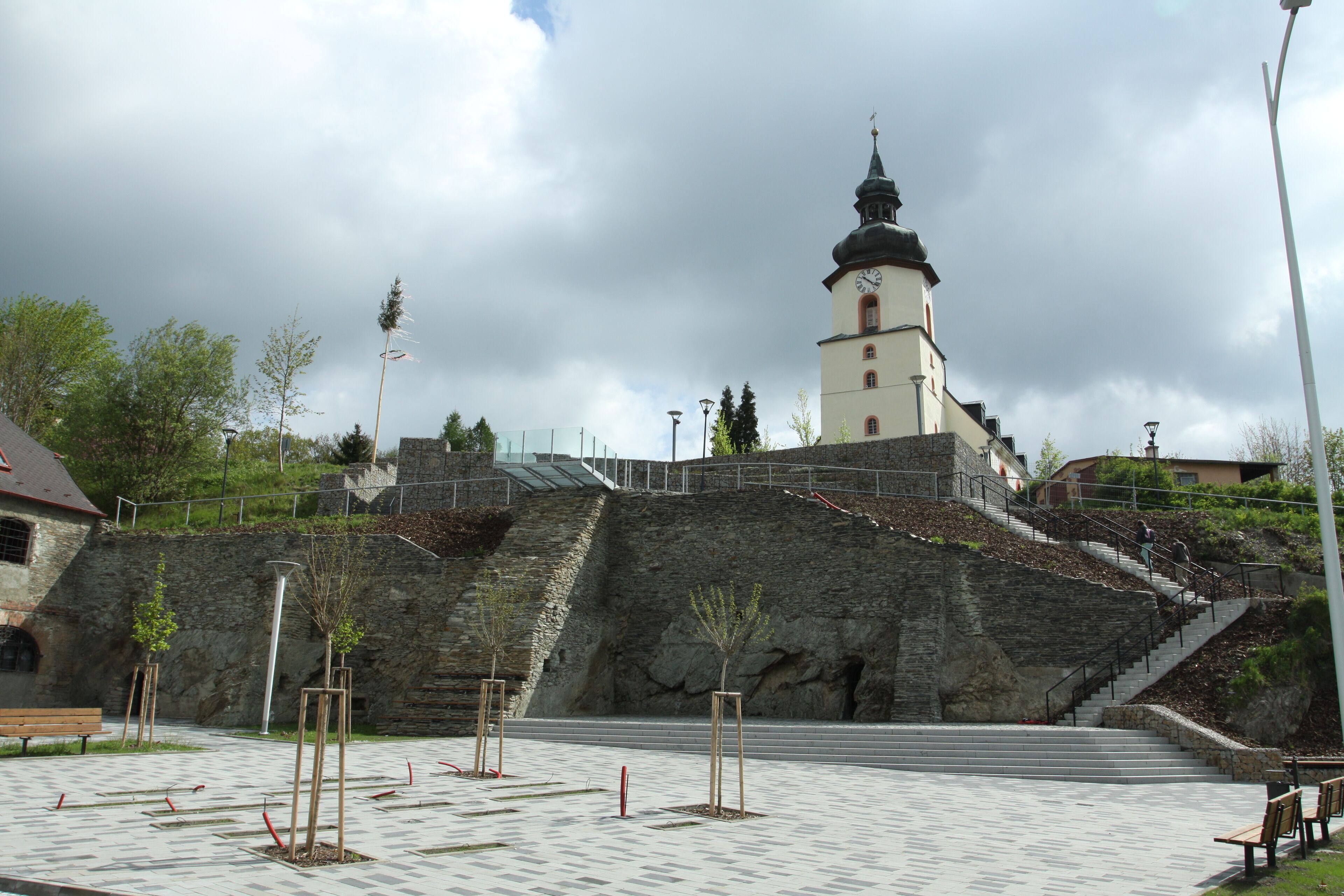A historic building with a clock tower, stone steps, and a paved plaza with benches.