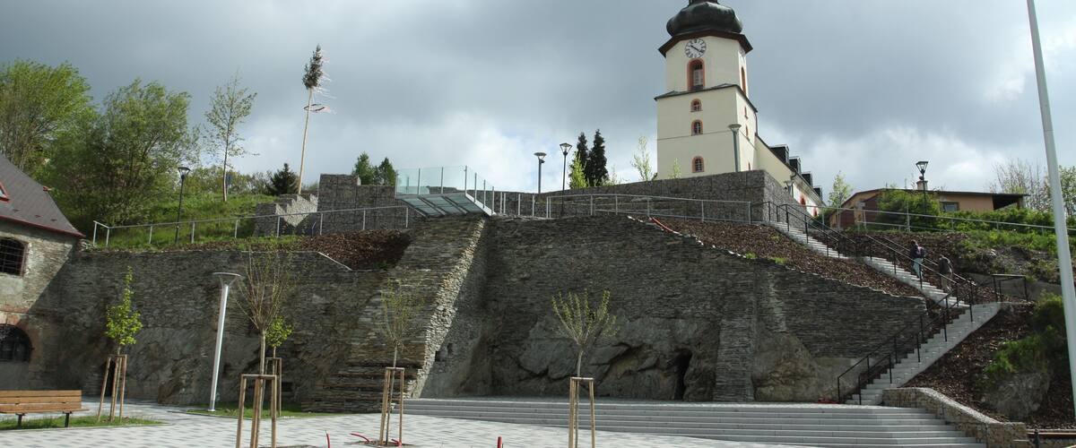 A historic building with a clock tower, stone steps, and a paved plaza with benches.