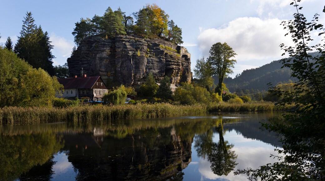 A calm river reflecting a rocky cliff and a traditional house with a red roof.