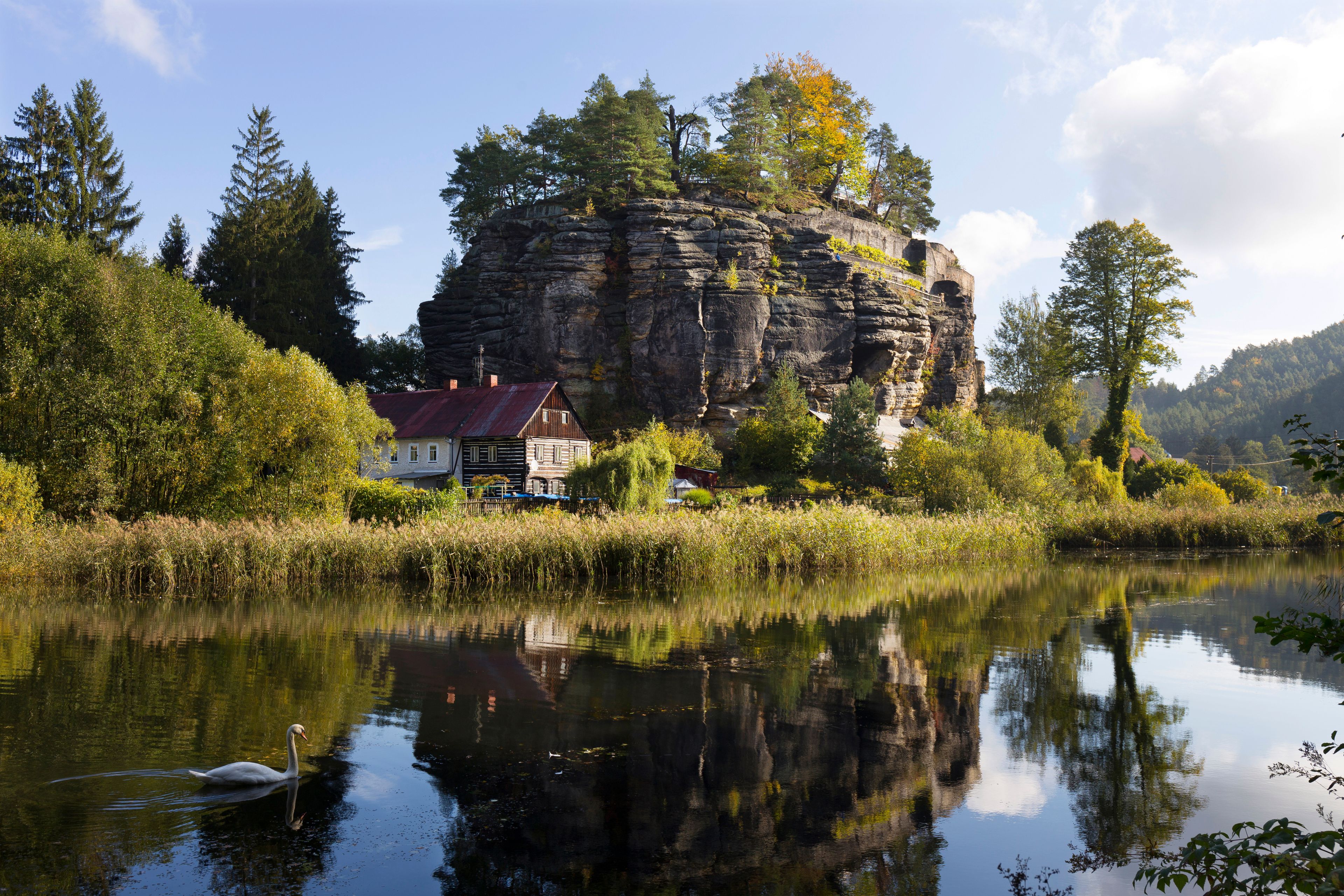 A house on a cliff by a calm river with reflections.