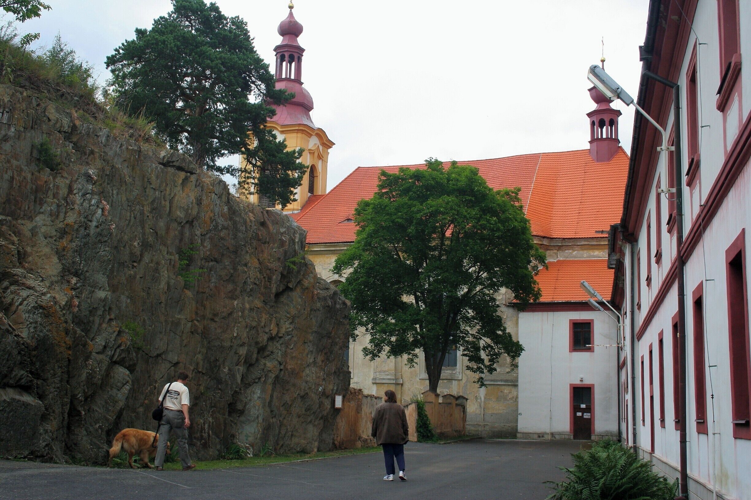 A rocky cliff, a building with red-tiled roof, and a person walking a dog.