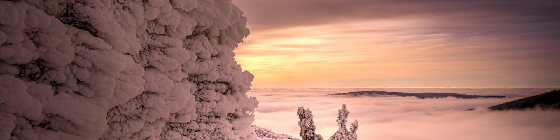 Paisagem coberta de neve com uma grande formação de gelo e um pôr do sol ao fundo.