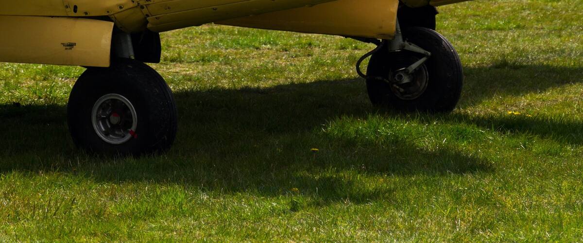 A small, single-engine aircraft with a red and yellow color scheme parked on grass.