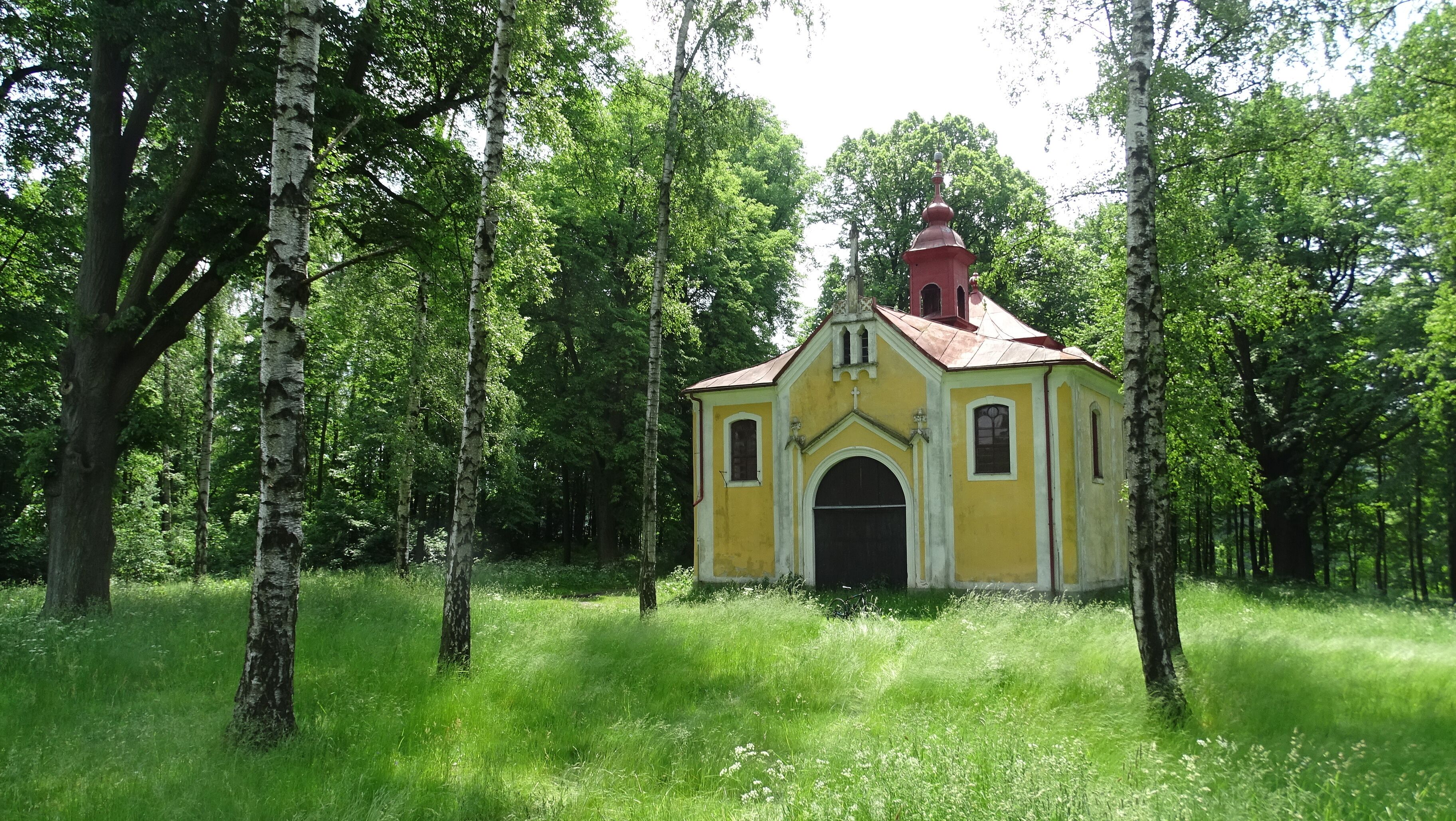 A small yellow church surrounded by lush green trees.