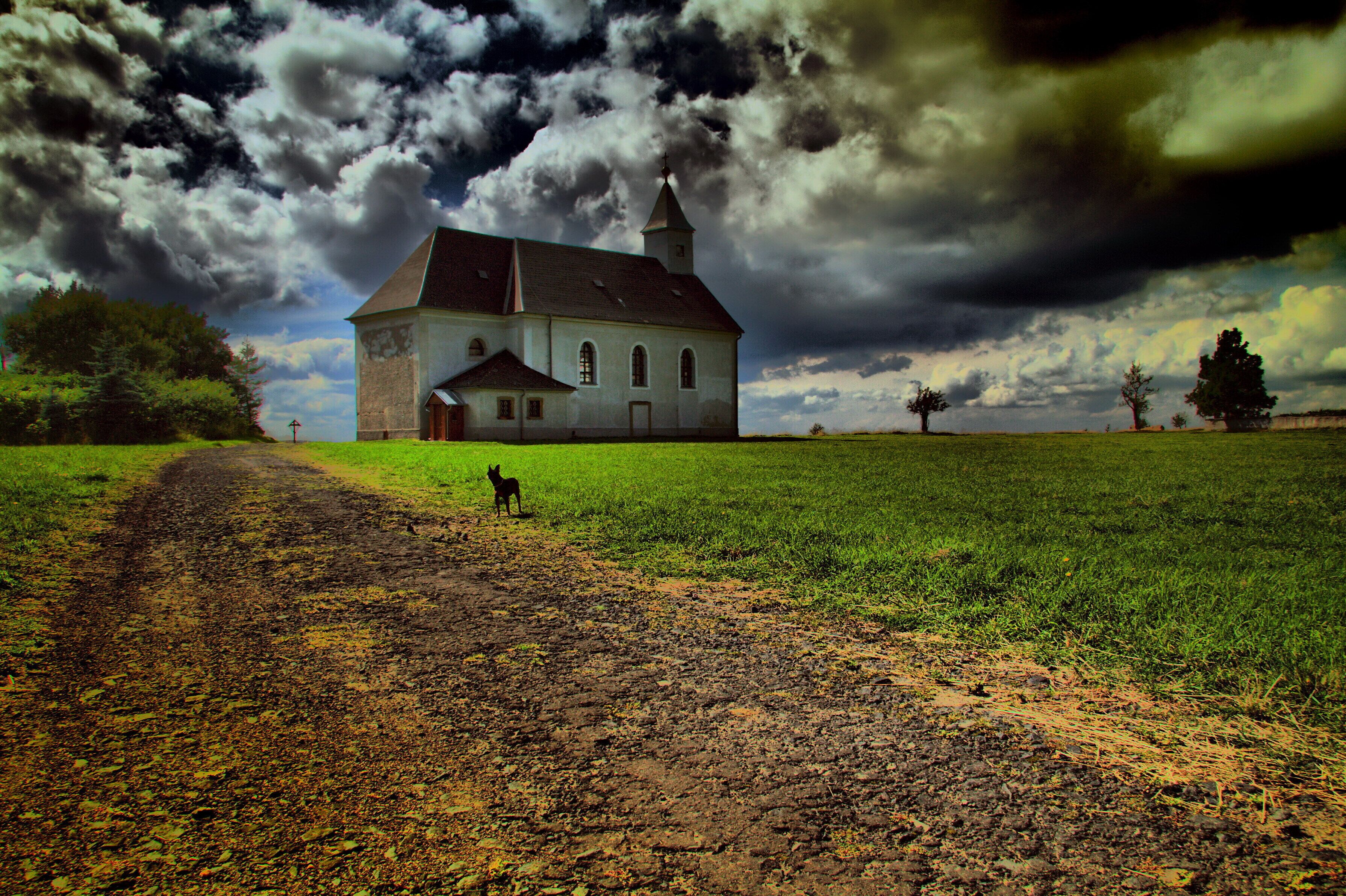 A church with a tall steeple in a grassy field under a stormy sky.