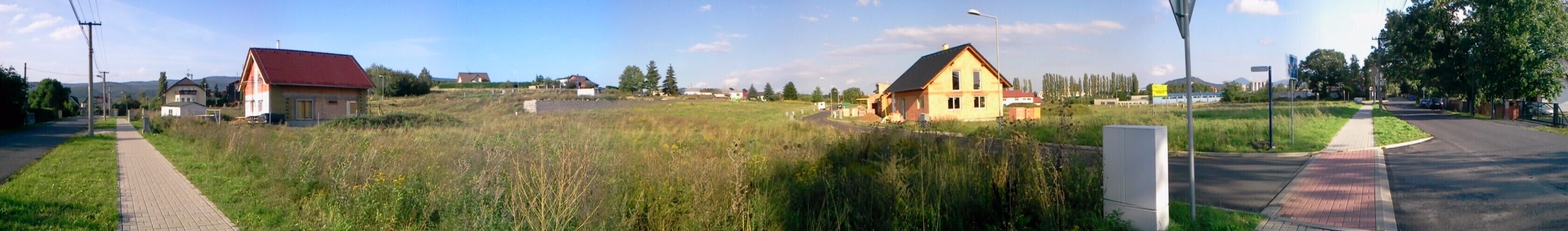 A rural landscape with a paved path, a grassy field, and two houses with red roofs.