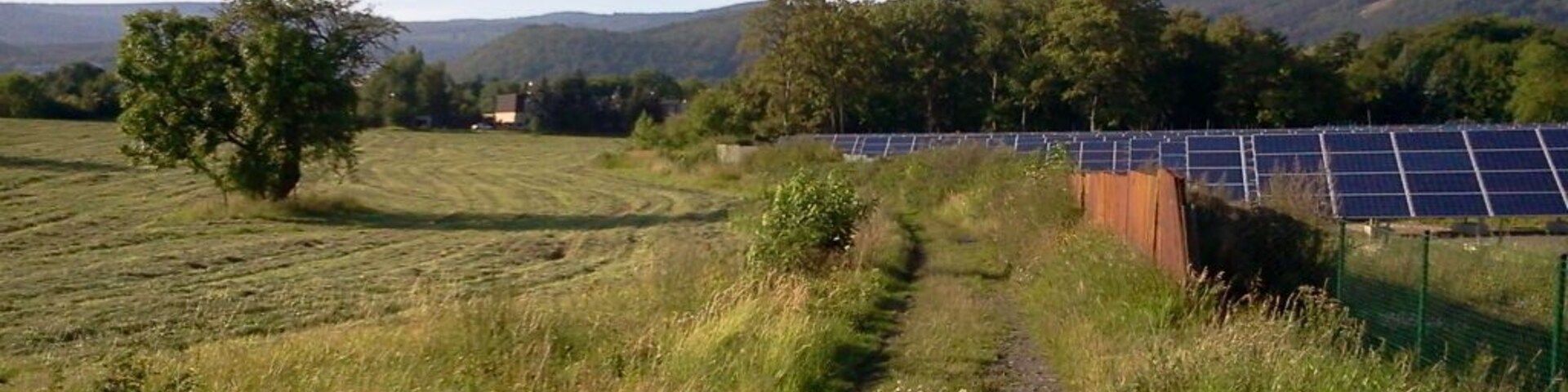 Paisaje rural con un camino de tierra que lleva a paneles solares.