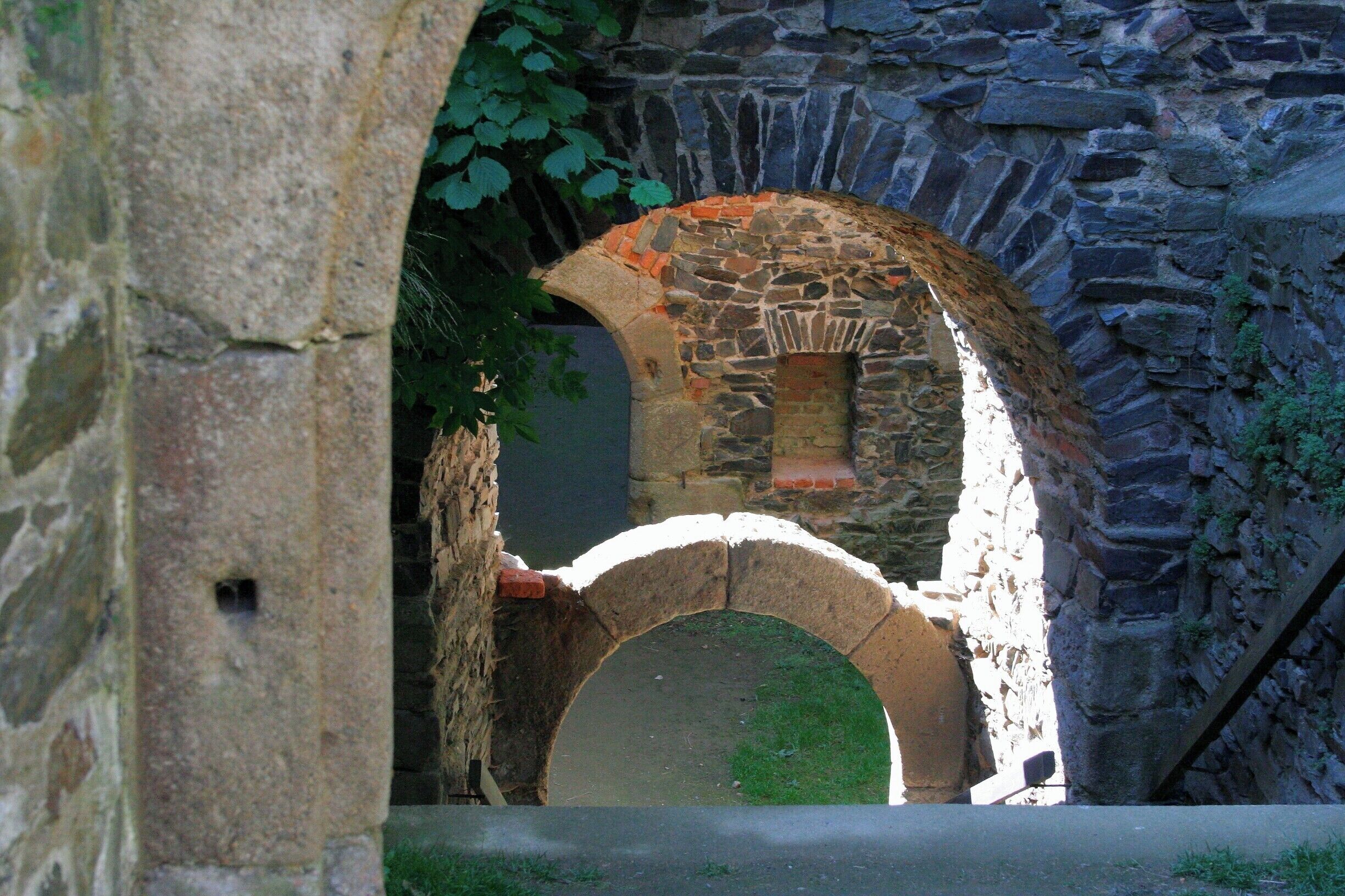 A stone archway leading to a stone building with a small window.