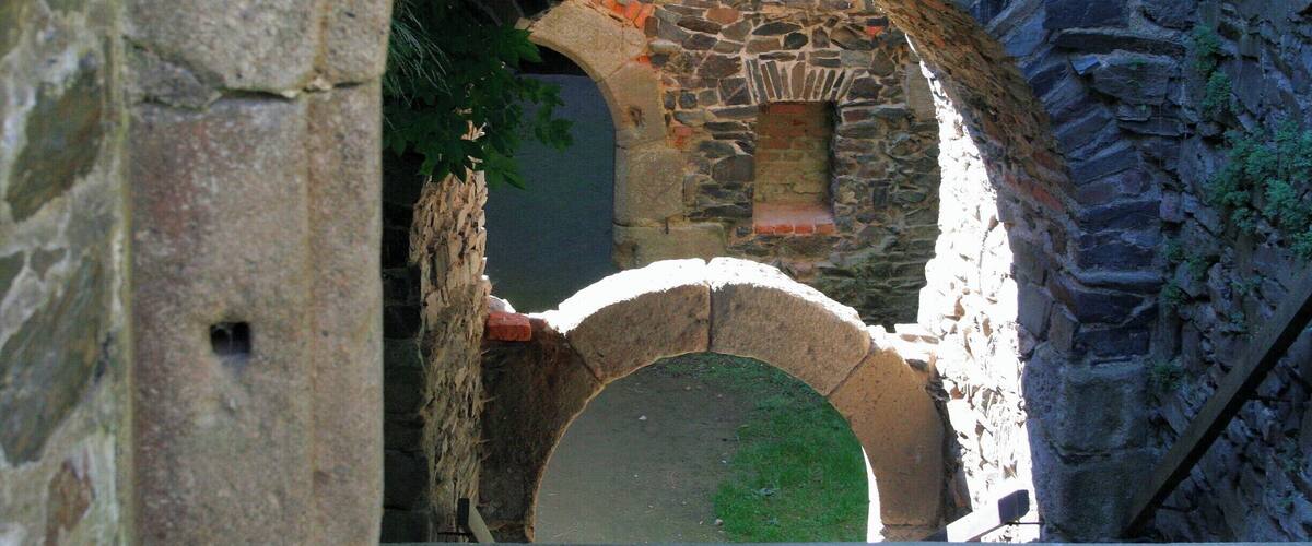 A stone archway leading to a stone building with a small window.