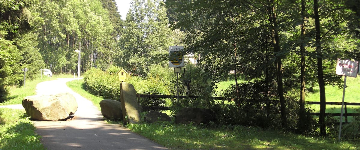 A narrow road with a wooden fence on one side and dense trees on the other.