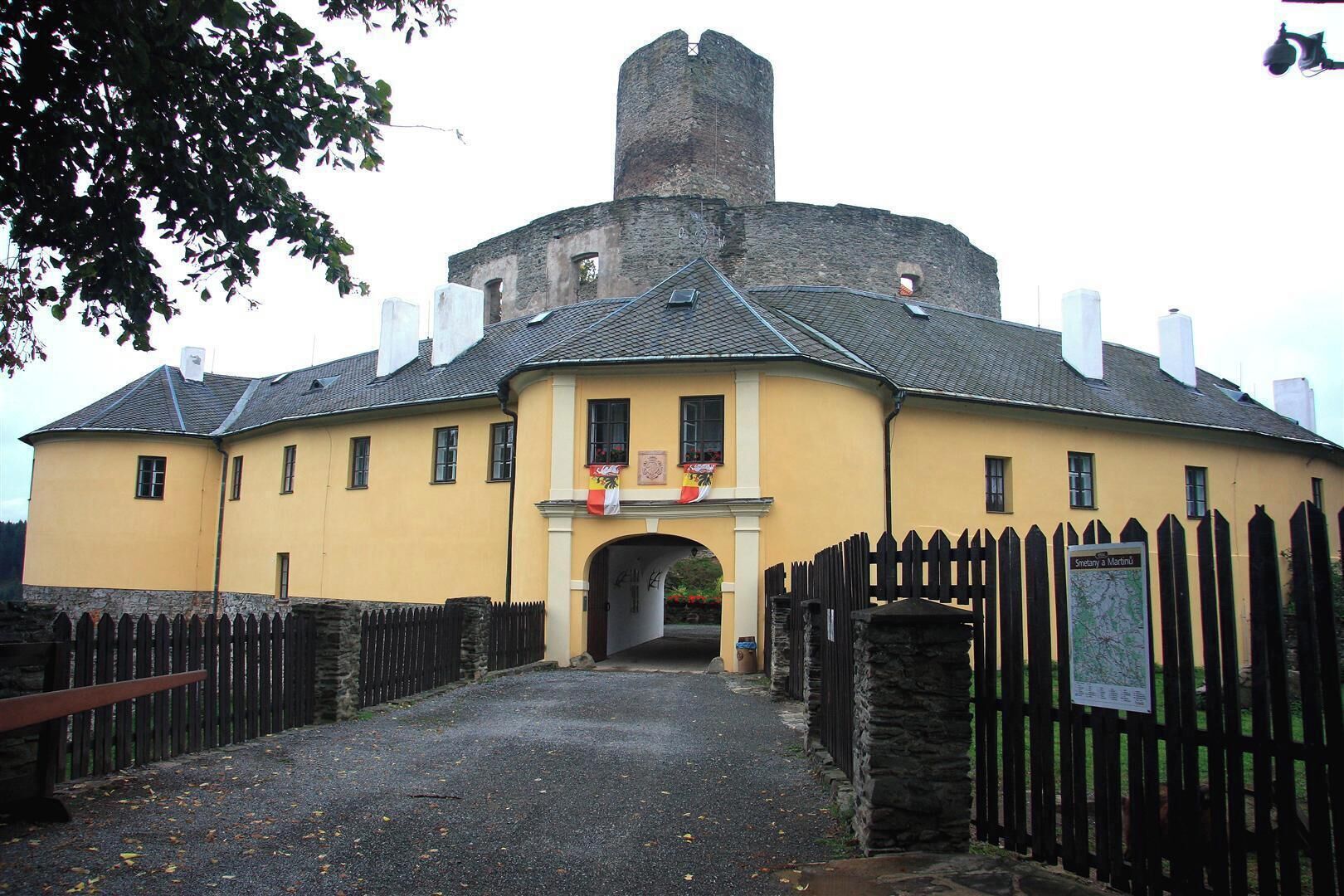 A historic building with a central tower, a yellow facade, and a wooden fence.