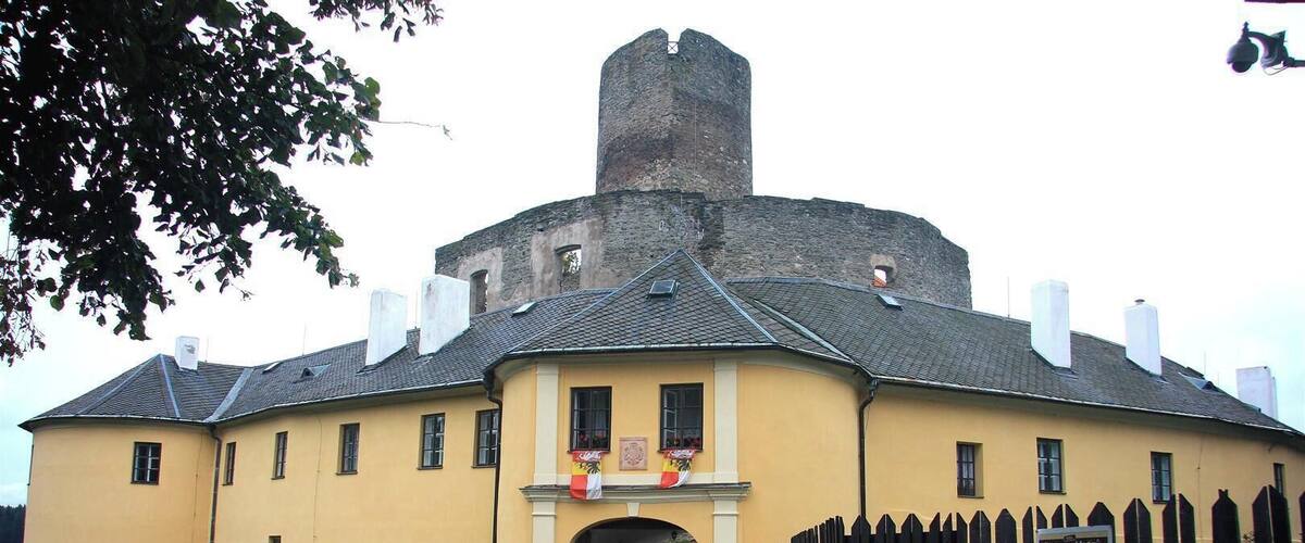 A historic building with a central tower, a yellow facade, and a wooden fence.