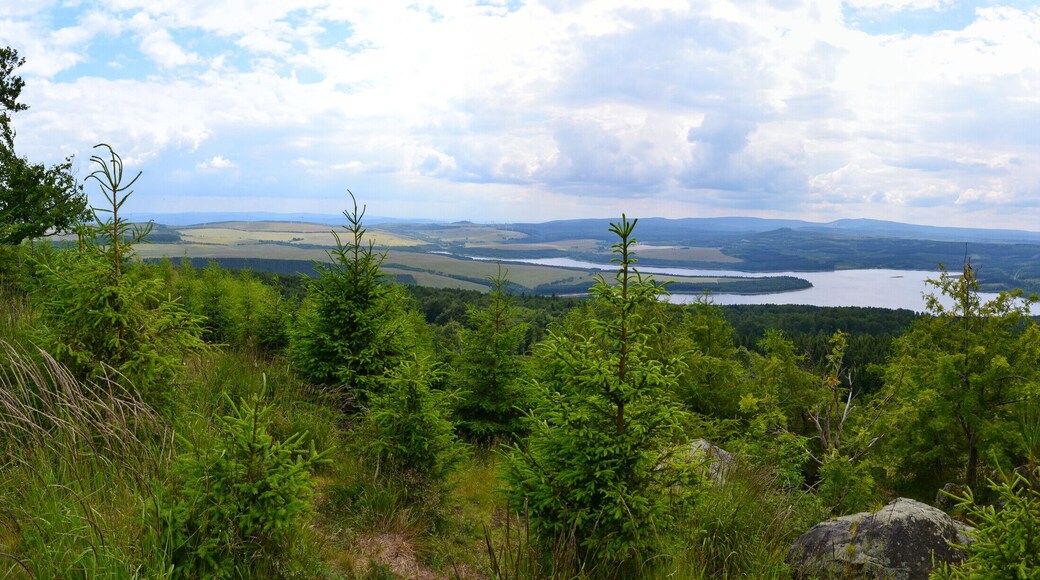 Panoramablick vom Gipfelrand des Jelení hora von Süden nach Nordwest. Im Hintergrund ist das Fichtelberg-Keilberg-Massiv, davor der Velký Špičák und im Vordergrund Stausee sowie Damm der Talsperre Preßnitz erkennbar. Unterhalb des Dammes liegt die Ortschaft Kryštofovy Hamry. Im Süden lässt sich zudem der Mědník sowie der Steilabbruch des Gebirges zum Egergraben hin erkennen.
