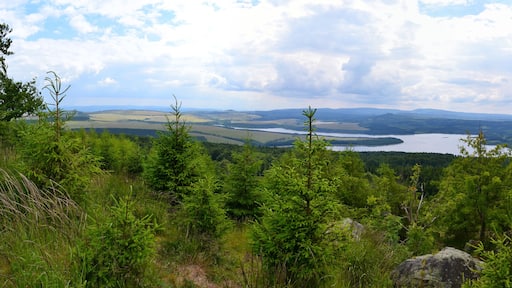 Panoramablick vom Gipfelrand des Jelení hora von Süden nach Nordwest. Im Hintergrund ist das Fichtelberg-Keilberg-Massiv, davor der Velký Špičák und im Vordergrund Stausee sowie Damm der Talsperre Preßnitz erkennbar. Unterhalb des Dammes liegt die Ortschaft Kryštofovy Hamry. Im Süden lässt sich zudem der Mědník sowie der Steilabbruch des Gebirges zum Egergraben hin erkennen.