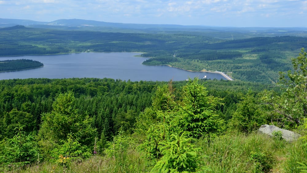 Ein See, umgeben von dichtem Wald und sanften Hügeln.
