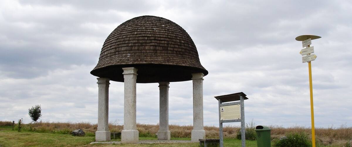 A gazebo with a dome roof and columns, surrounded by grass and a path.