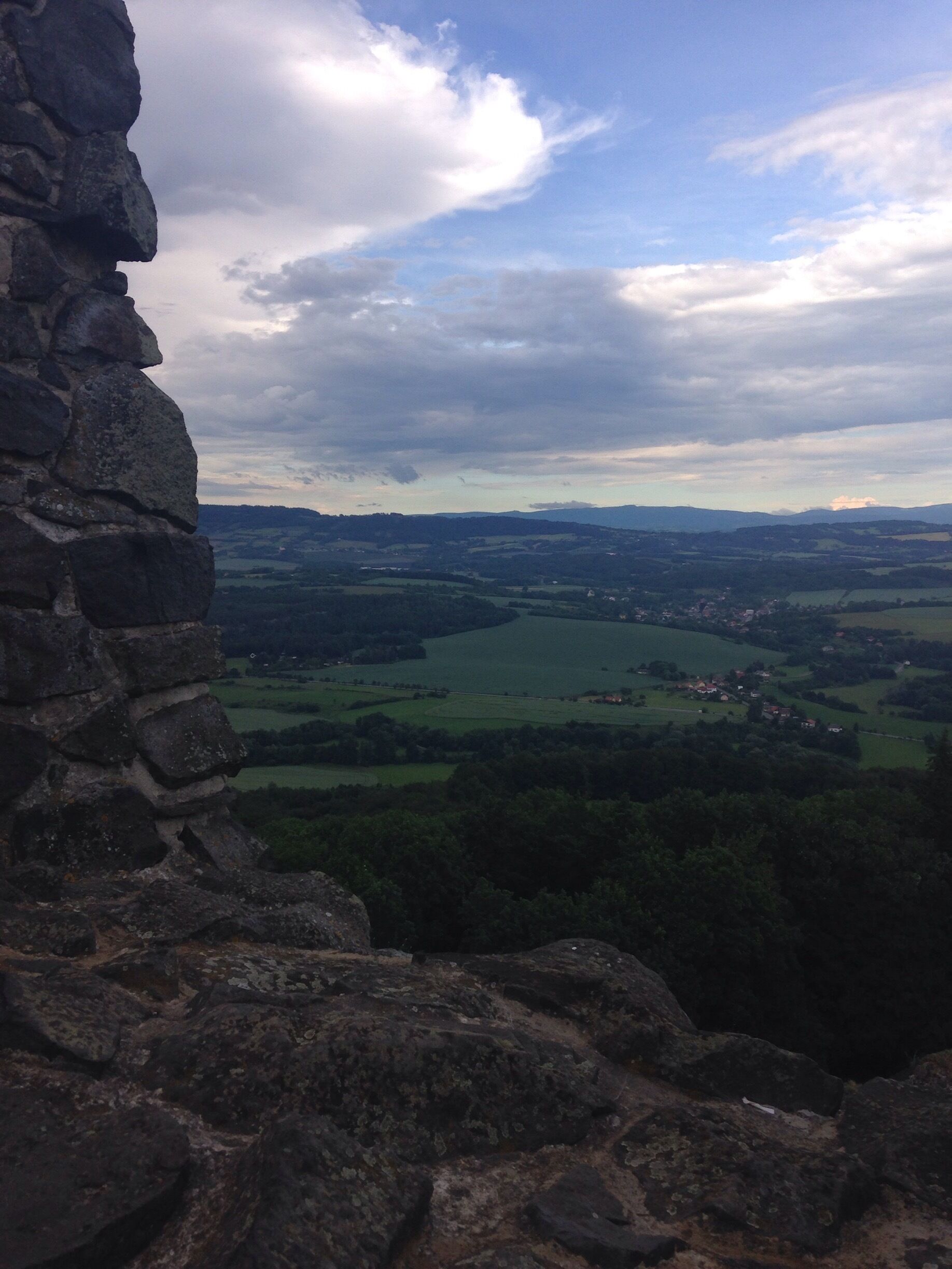 A stone wall overlooking a valley with fields and distant mountains.
