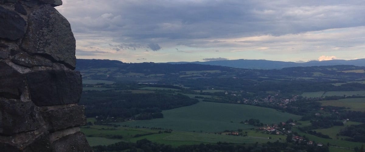 A stone wall overlooking a valley with fields and distant mountains.