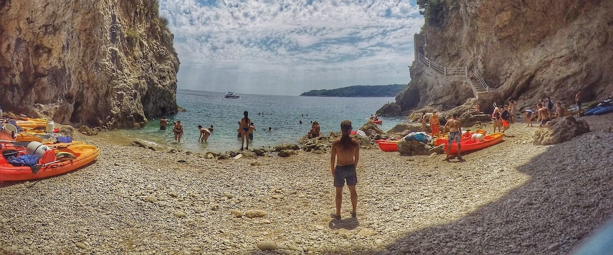 A rocky beach with a clear sky and a boat in the water.