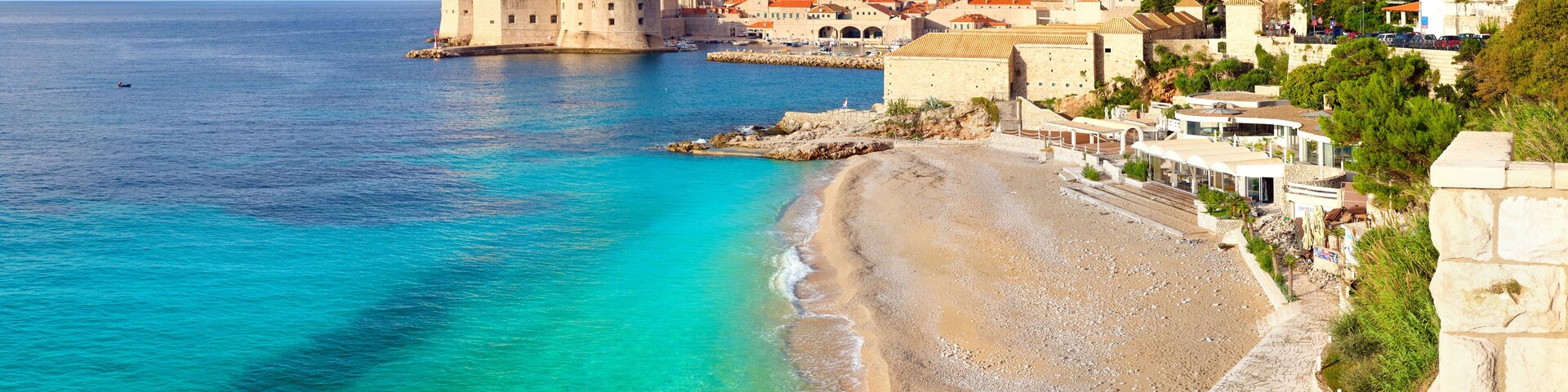 Eine Küstenstadt mit einer historischen Festung, klarem türkisblauem Wasser und einem Kiesstrand.