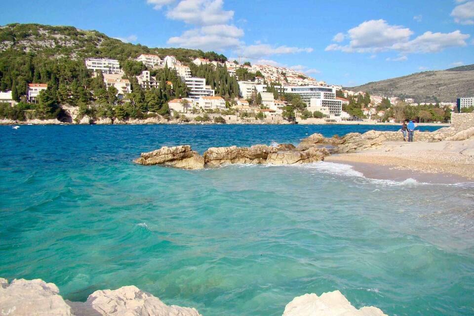 A coastal town with clear blue waters, rocky outcrops, and buildings on a hillside.
