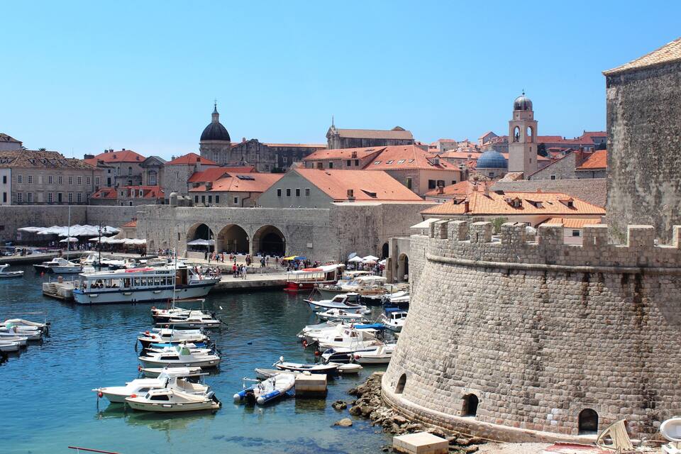 Un port històric amb embarcacions amarrades, una torre rodona destacada i un edifici amb cúpula al fons.
