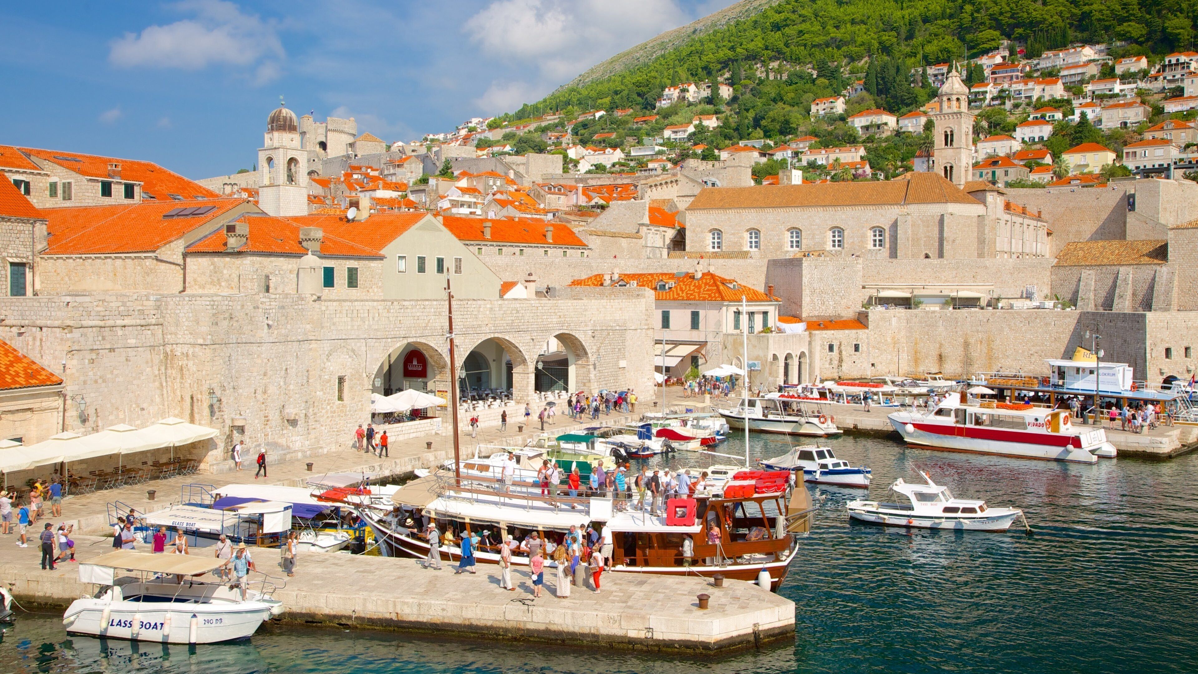 A harbor with boats, a stone building, and a hillside with houses.