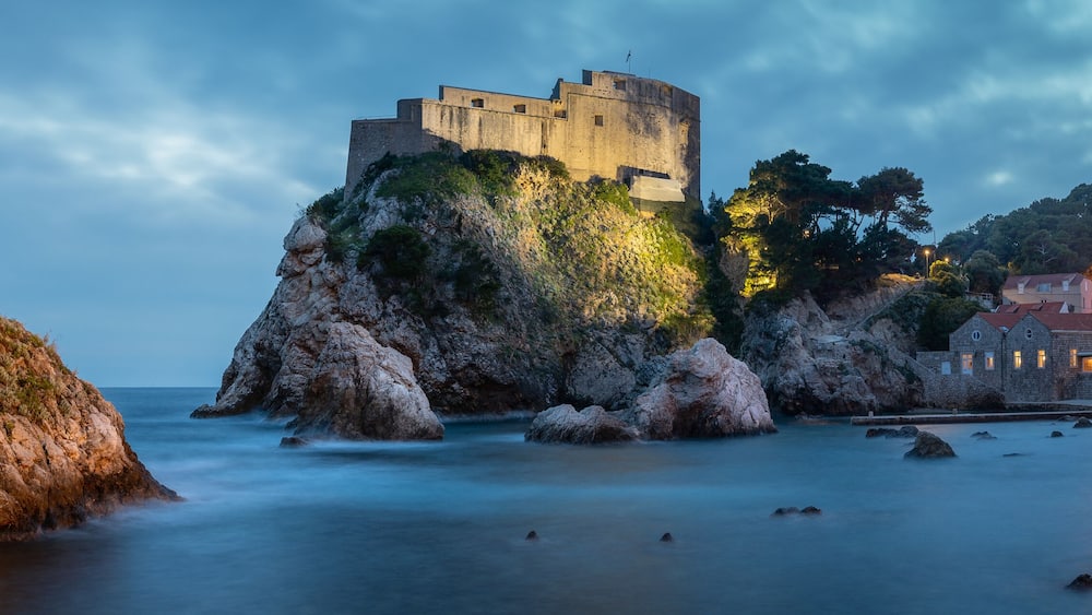 Une tour de pierre historique et un château fortifié, tous deux situés sur un promontoire rocheux en bord de mer.