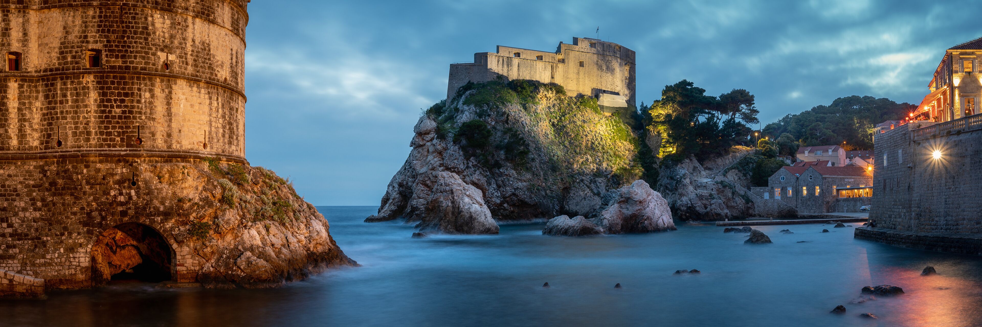 A historic stone tower and a fortified castle on a rocky outcrop by the sea.
