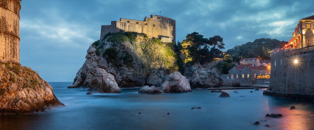 A historic stone tower and a fortified castle on a rocky outcrop by the sea.