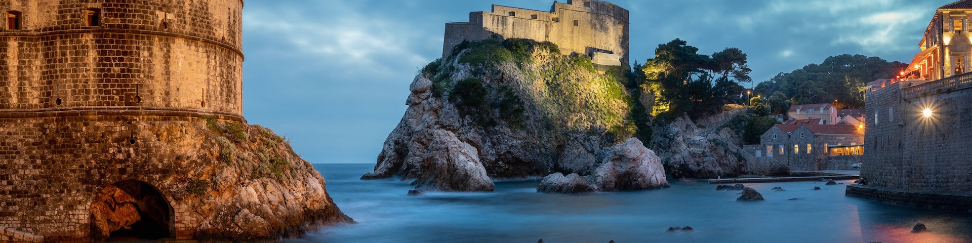 A historic stone tower and a fortified castle on a rocky outcrop by the sea.